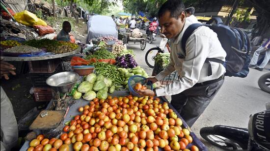 A man buys tomato near Ranjeet Singh flyover in Delhi on Tuesday. Tomato prices have risen in the city due to rains. (Sanjeev Verma/HT photo)