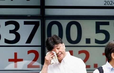 A passerby gestures in front of an electronic board displaying the Nikkei stock average outside a brokerage in Tokyo, Japan. (Reuters)