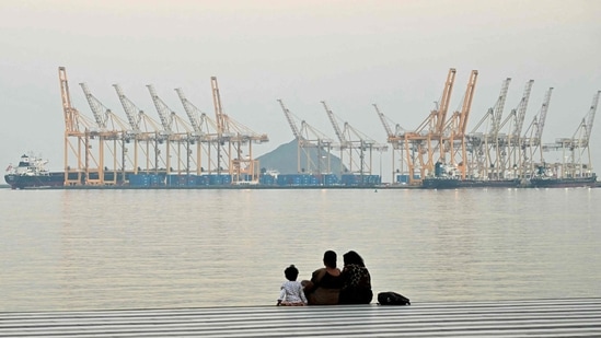 A family sits against the backdrop of a dockyard off coast city of Fujairah, in the Strait of Hormuz in the northern Emirate on 25 February 2026. (AFP)