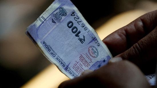 A customer holds  ₹100 notes near a roadside currency exchange stall in New Delhi. (Reuters)