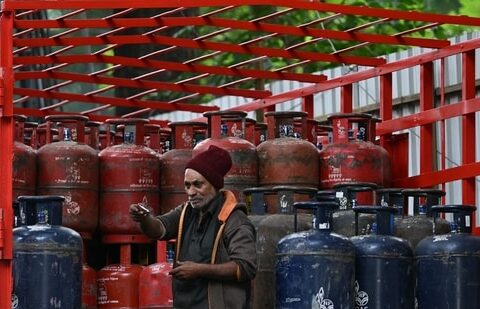 A delivery worker stands atop a truck carrying LPG cylinders at a HP Gas distribution point in Bengaluru. (AFP)